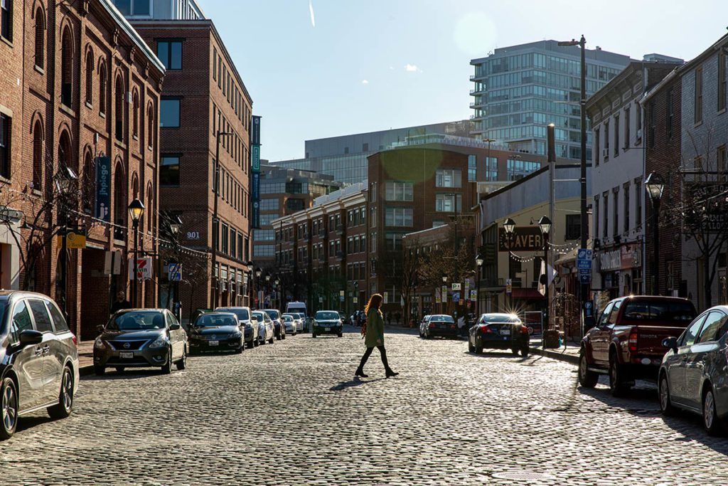A woman walks across a cobblestone street in Fell's Point, a scenic neighborhood in Baltimore, an affordable event destination with charm.