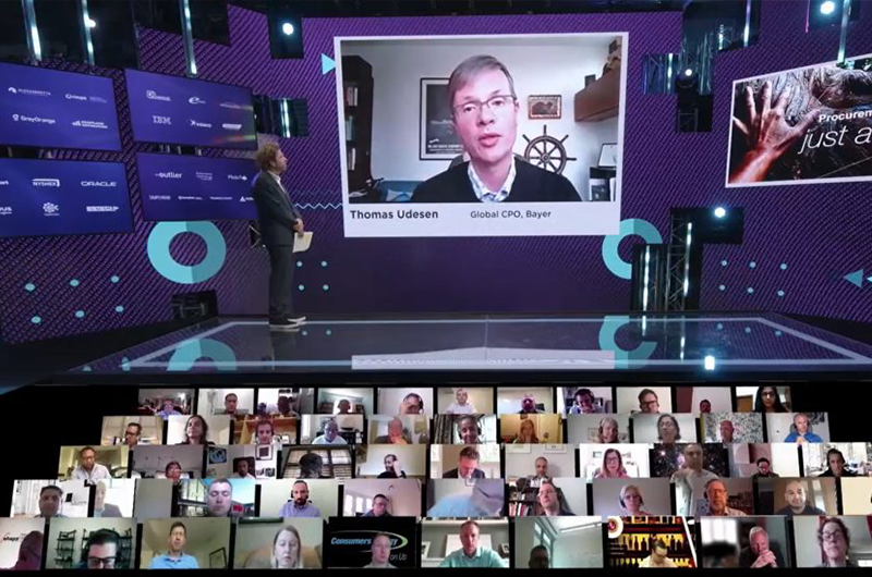 A view of a presentation at a business event, with both an in-person emcee and virtual participants visible on specialized screens.