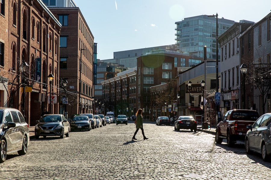 A woman walks across a cobblestone street with low-rise nineteenth-century and early-twentieth-century brick buildings on either side, offset with old-fashioned cast iron street lights. These kinds of eclectic neighborhoods can make tech hubs particularly attractive for meetings and events.