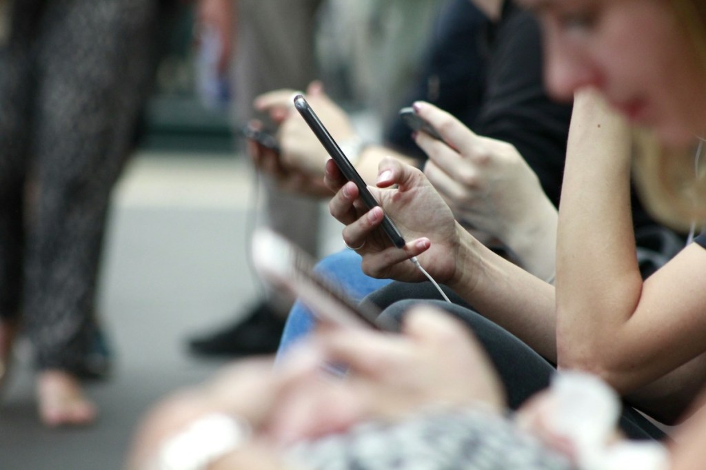 Person holding a smartphone at an event sitting in a row of chairs